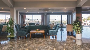 A hotel lobby with a green sofa, chairs, a small table with a flower arrangement, potted plants, and a view of the mountains through large windows. - Dalya Resort Aqua & Spa Hotel (Datça)