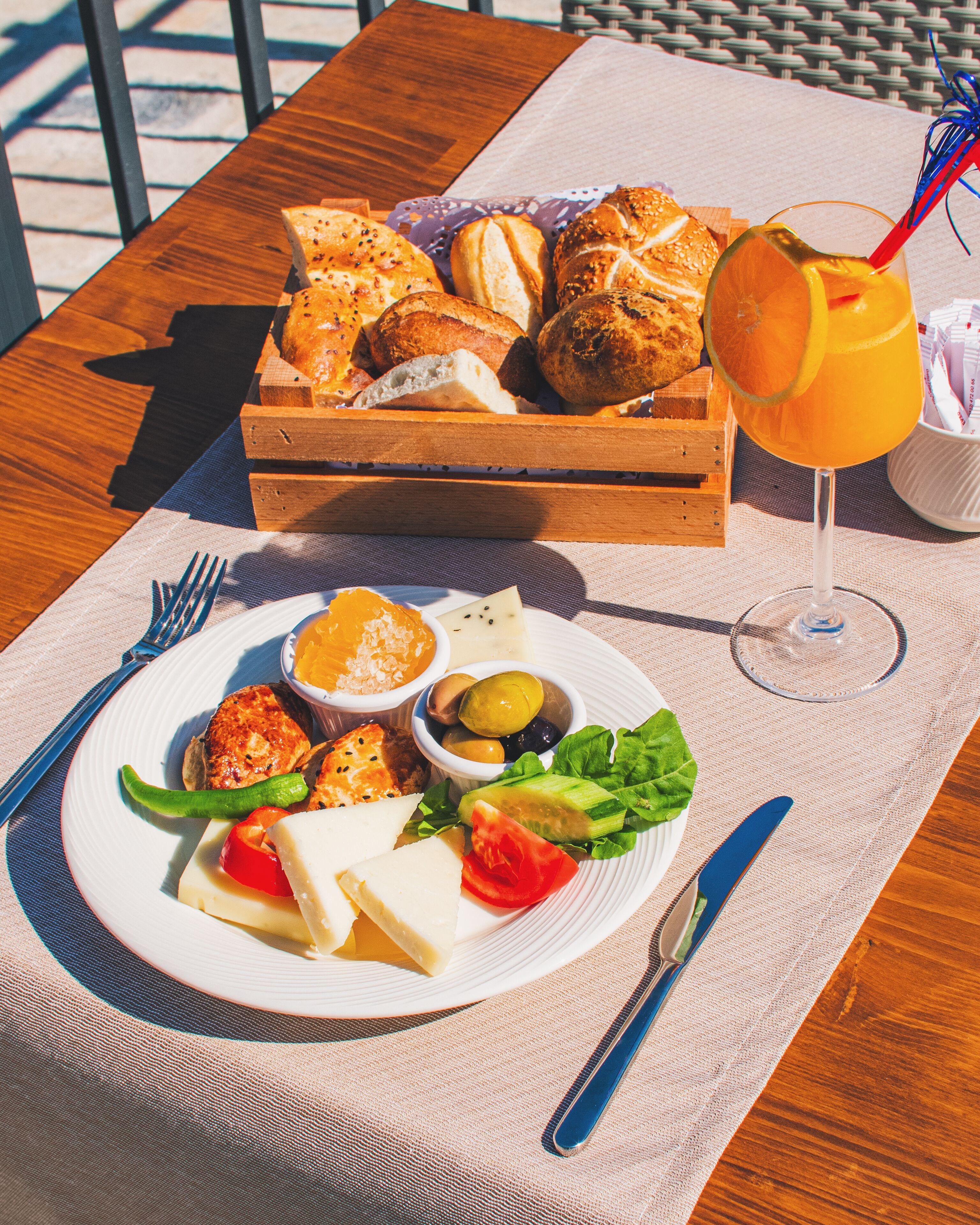A wooden table with a plate of food, a basket of bread, and a glass of orange juice.