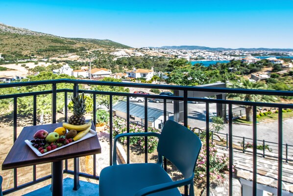 A balcony with a table holding fruit and a chair, overlooking a coastal town with houses and a body of water. - Dalya Resort Aqua & Spa Hotel (Datça)