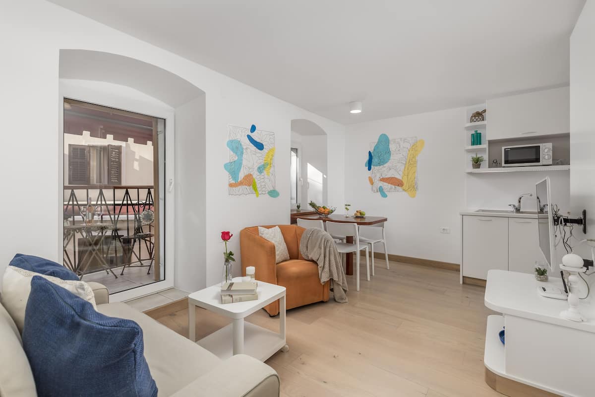 Una sala de estar moderna con sofá, mesa de centro y comedor con mesa y sillas. Hay una zona de cocina con microondas y armarios.