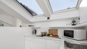 Una cucina compatta con un lucernario, mobili bianchi, un forno a microonde e un lavandino.