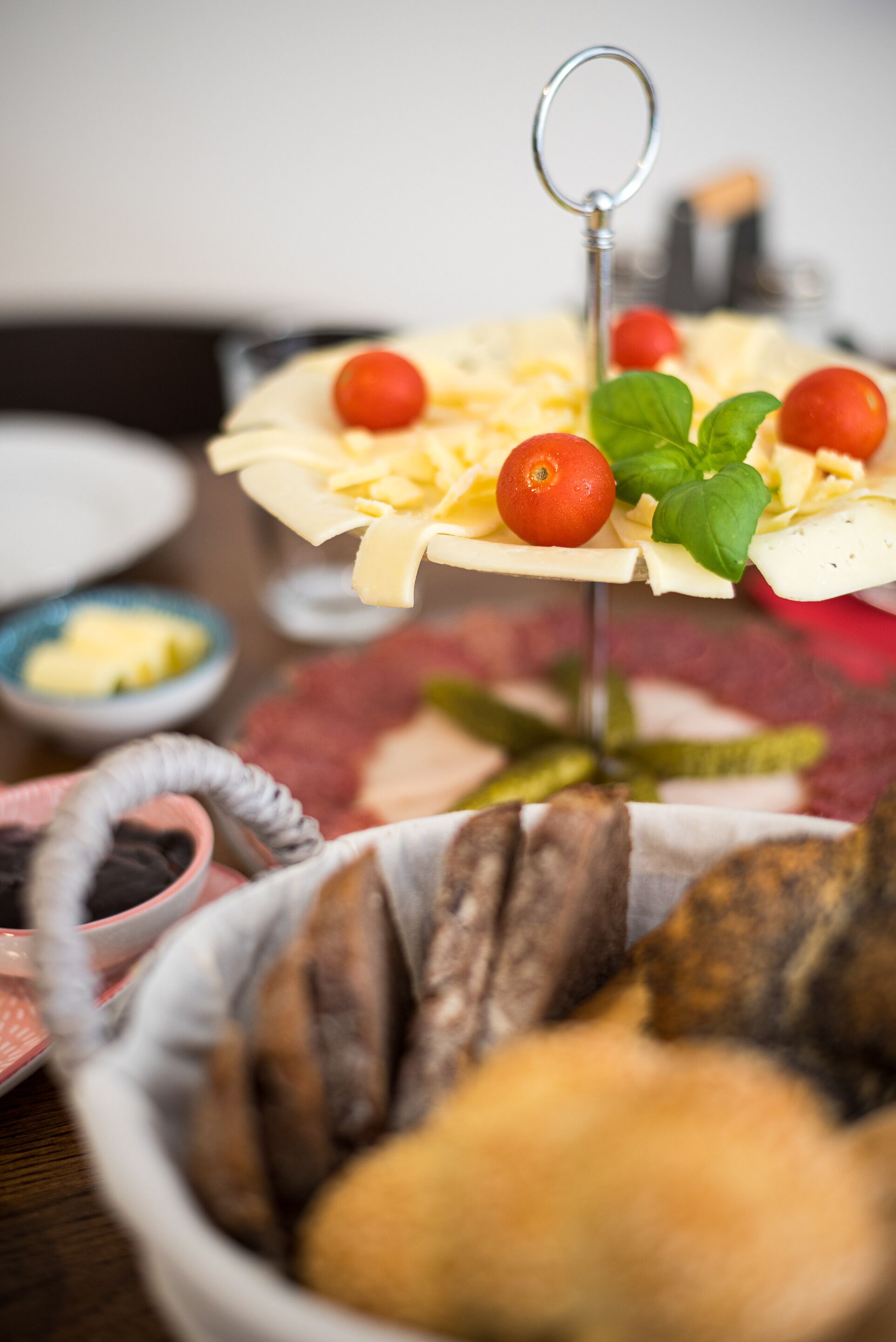 A charcuterie board with various cheeses, tomatoes, and basil leaves, accompanied by bread and pickles.
