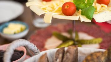 A charcuterie board with various cheeses, tomatoes, and basil leaves, accompanied by bread and pickles.
