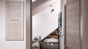 A bedroom with a bed, a nightstand, a wall-mounted shelf, a framed text on the wall, and a door.