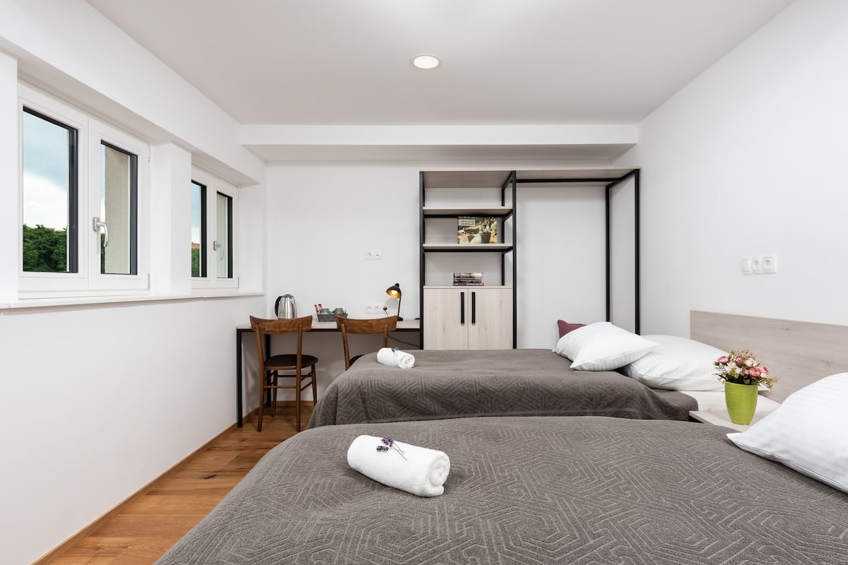 A modern hotel room with two beds, a desk, and a cabinet.