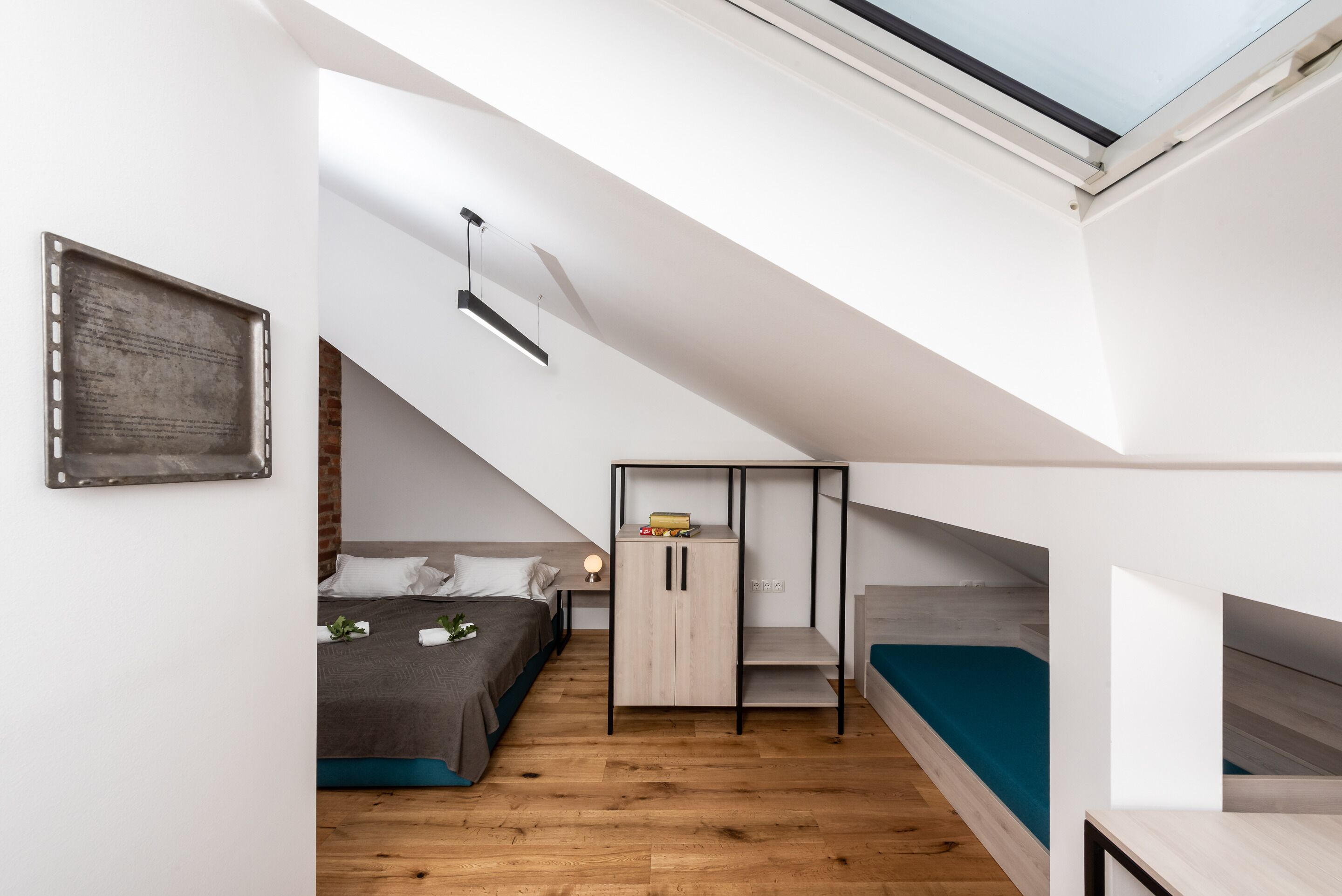 Ein kompakter, moderner Schlafraum mit geneigter Decke, einem Dachfenster, einem Bett, einem Kleiderschrank und einer kleinen Sitzecke.