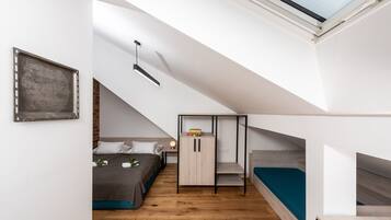 Ein kompakter, moderner Schlafraum mit geneigter Decke, einem Dachfenster, einem Bett, einem Kleiderschrank und einer kleinen Sitzecke.