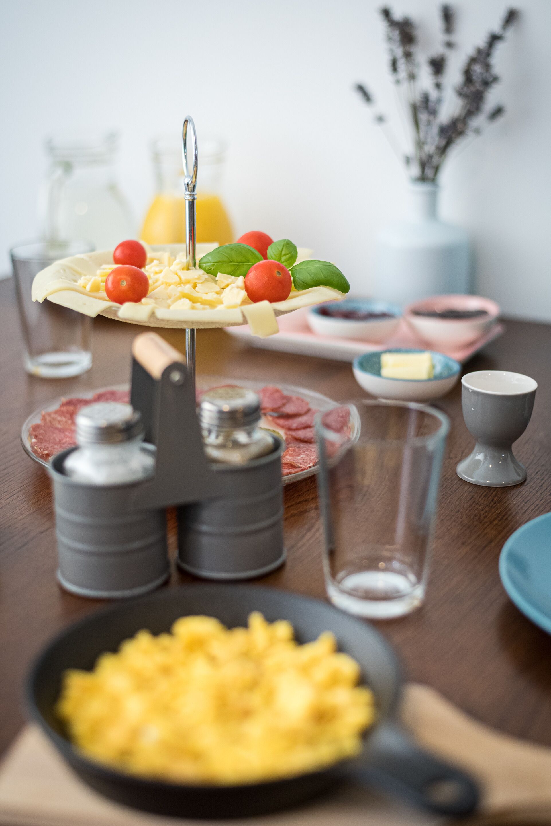 A breakfast setting with a pizza, tomatoes, basil, and a cheese spread on a stand.