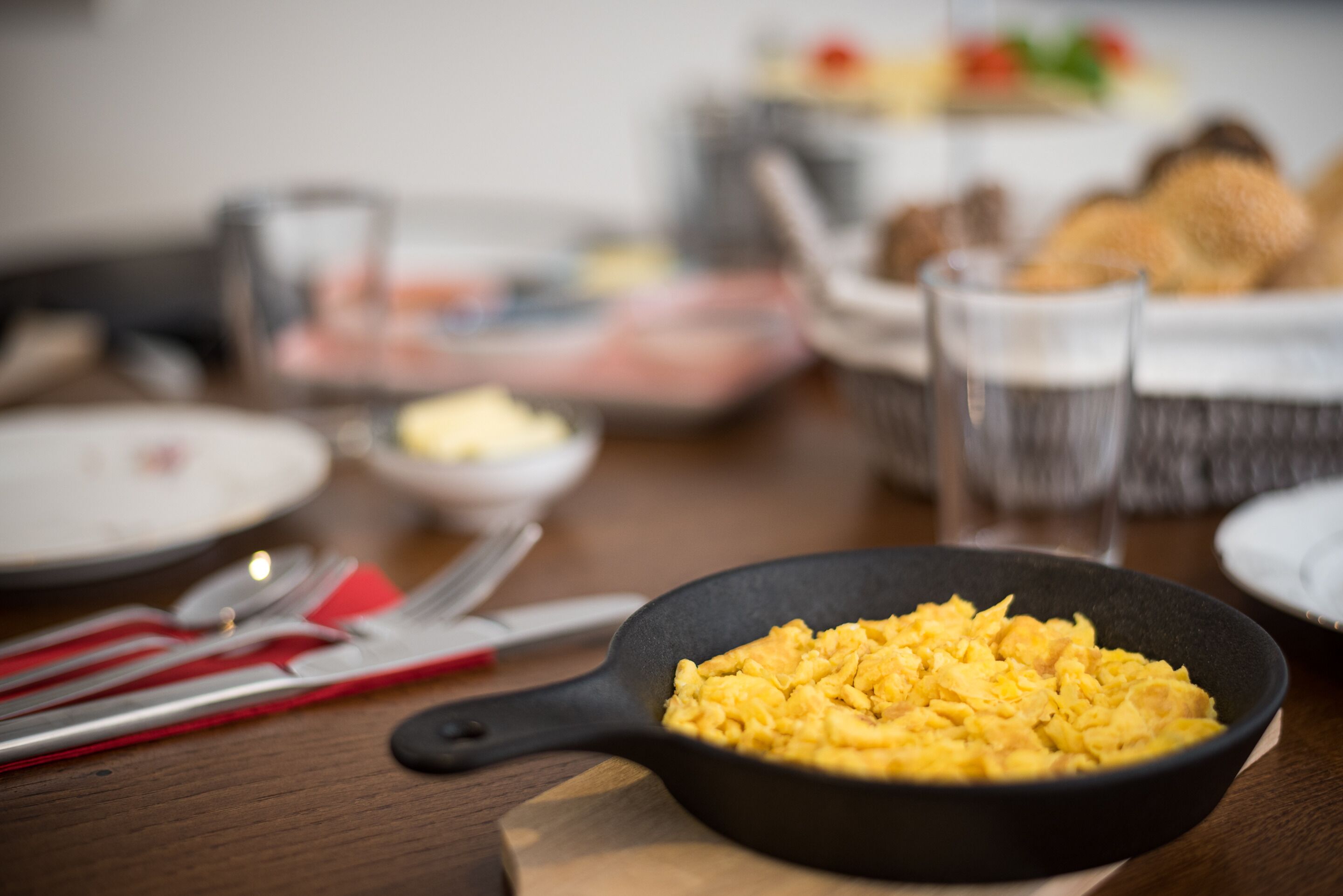 A dining table with a black skillet containing scrambled eggs, a glass of water, and various dishes in the background.