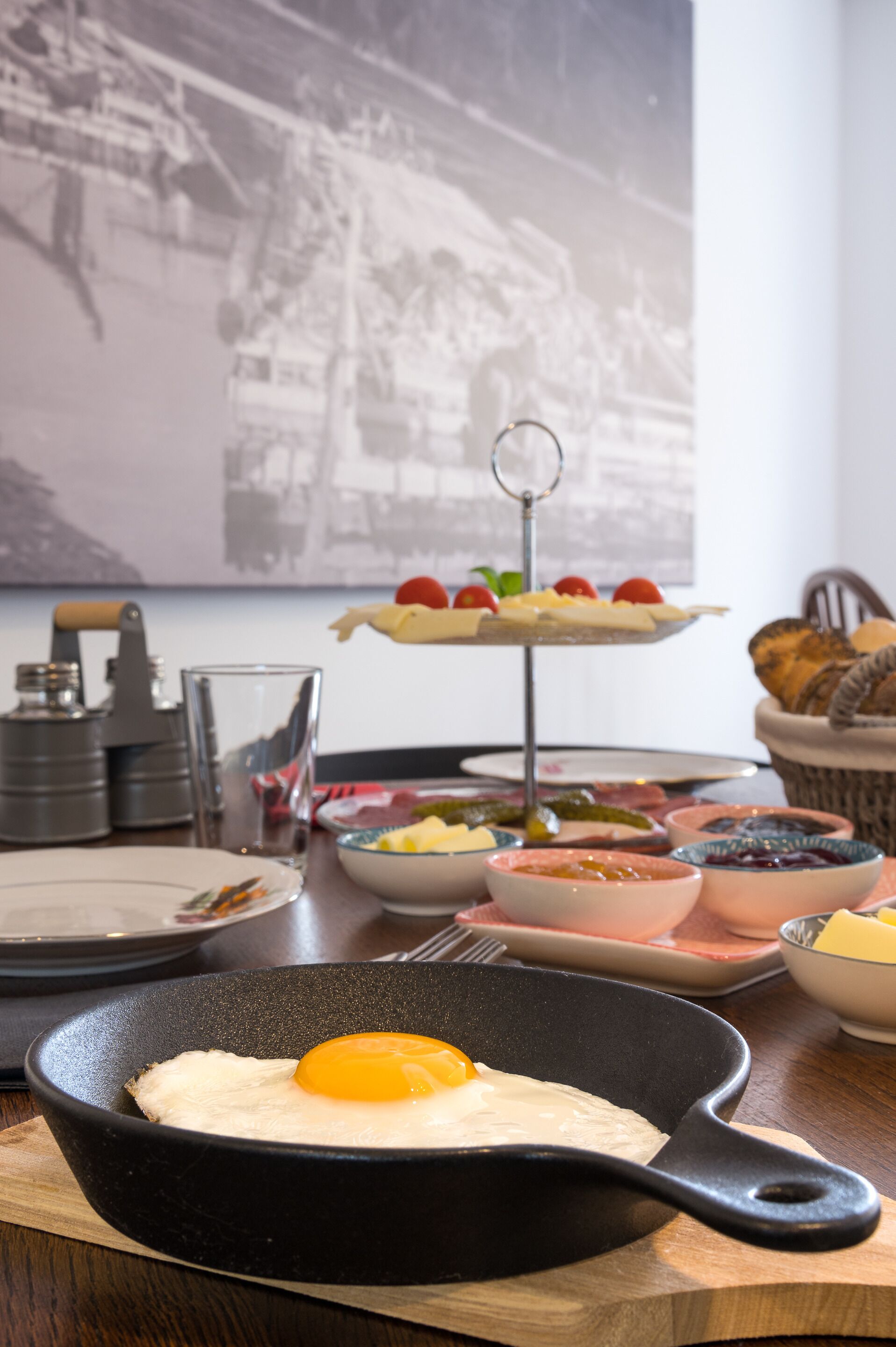 Une table mise pour le petit-déjeuner, avec une poêle contenant un œuf, un plateau de fruits et divers condiments.