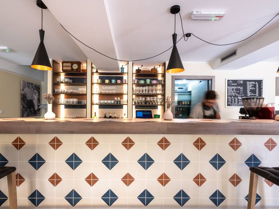 A bar area with a patterned tile backsplash, shelves with glasses, and pendant lighting.