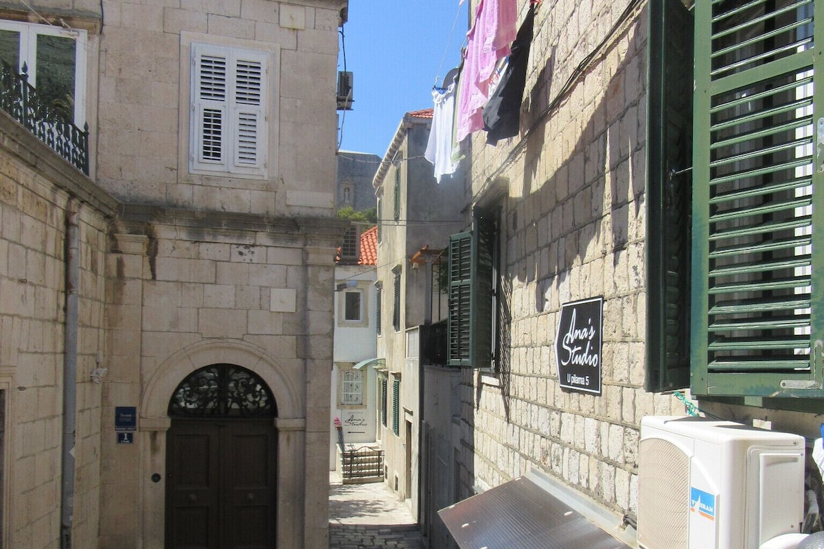 A narrow street with buildings on either side, a metal gate, and a sign for 'Ana's Studio'.