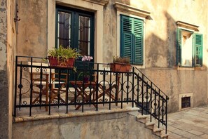 A stone building with a balcony featuring a wrought iron railing, potted plants, and a wooden table. - Pile Excellent Location Apartments (Dubrovnik)