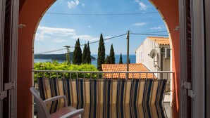 Ein Balkon mit Blick auf das Meer und Bäume, ein Stuhl und ein gestreifter Vorhang.