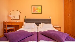 Ein Doppelbett mit violetten Kissen, ein Holztisch mit Stuhl, ein Spiegel und ein Nachttisch mit Lampe.