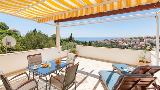 A terrace with a table, chairs, and a view of the sea and town. - Villa Mia (Dubrovnik)