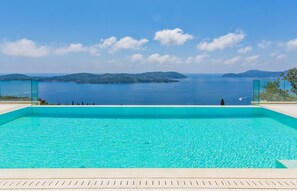Piscina azul e límpida com vista para o mar e ilhas ao longe.