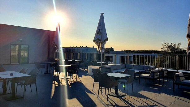 An outdoor terrace with tables and chairs, a flag, and a view of the sunset. - Hotel Adler (Münster)