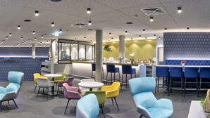 A modern hotel lobby with a bar area, colorful seating, and a patterned wall. - Hotel Adler (Münster)