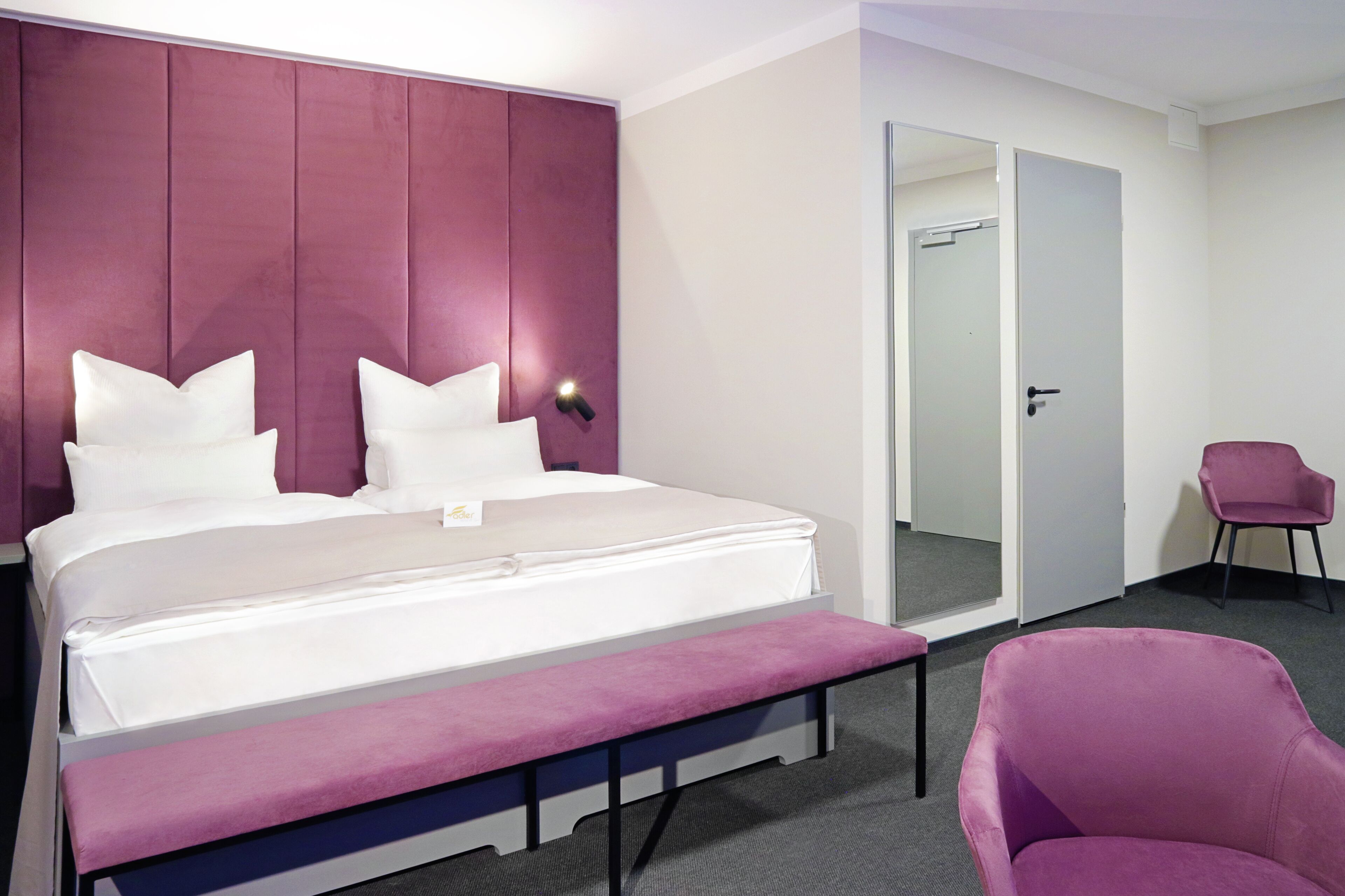 Una habitación de hotel con una cama grande, un banco, una silla y una puerta.