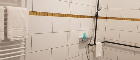 Une salle de bain avec des murs recouverts de carreaux blancs, un sol à carreaux, un porte-serviettes et un espace douche.