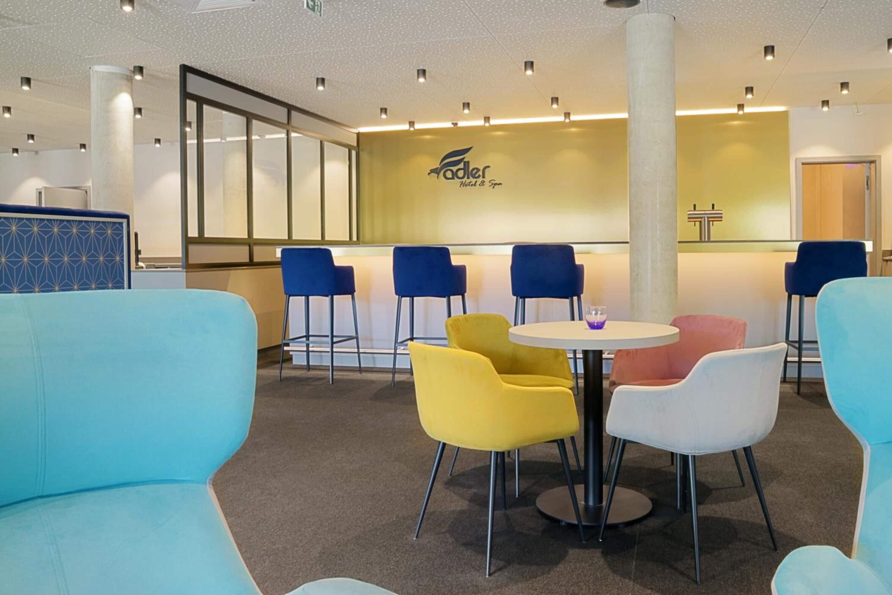 Een hotel lobby met een receptiebalie, blauwe en gele stoelen en een ronde tafel.