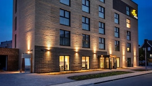 A modern hotel building with a brick facade, multiple windows, and a well-lit entrance. - Hotel Adler (Münster)