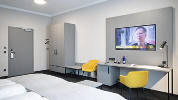 Una habitación de hotel con una cama, un escritorio, dos sillas amarillas, un televisor y un armario.