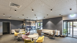 A modern lounge area with round tables and colorful chairs, a sofa, and a patterned wall. - Hotel Adler (Münster)