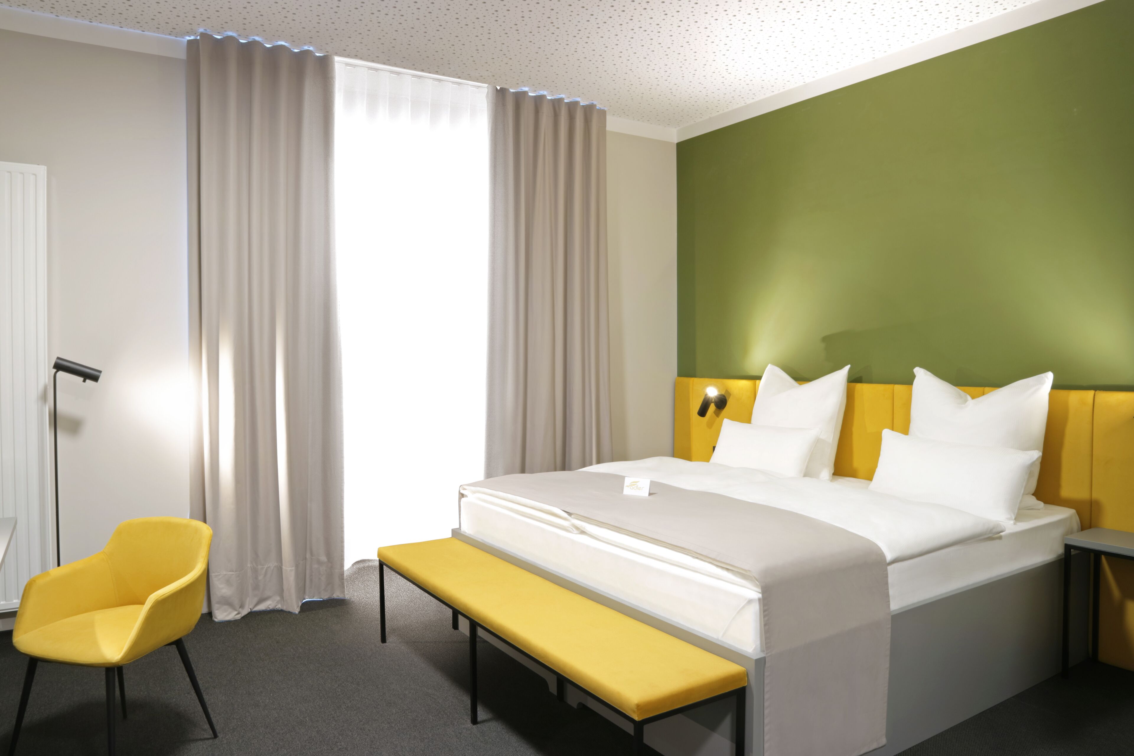 Una camera d'albergo con un letto, una panca, una sedia e una parete verde decorativa.