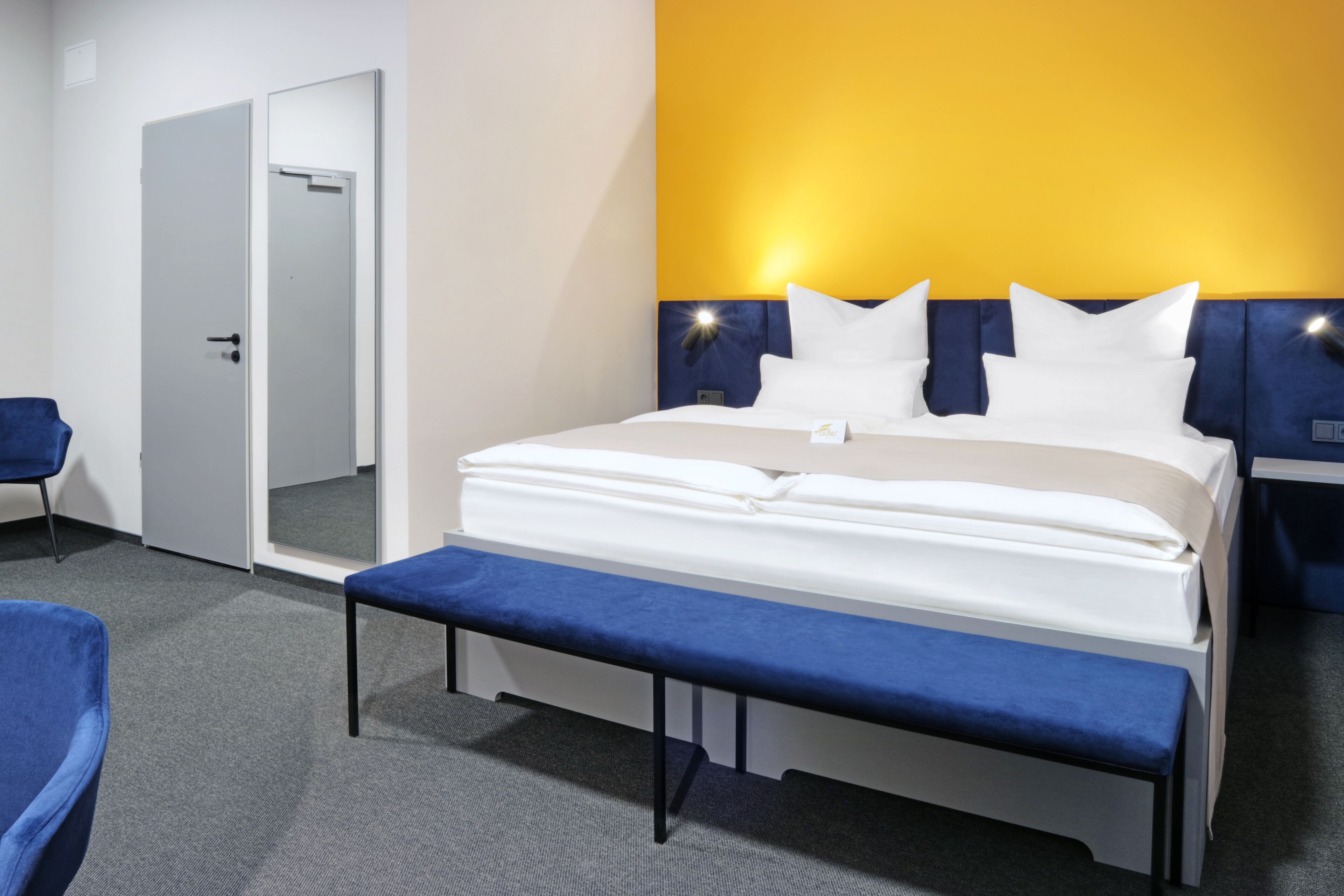 A hotel room with a bed, a bench, a chair, and a door.