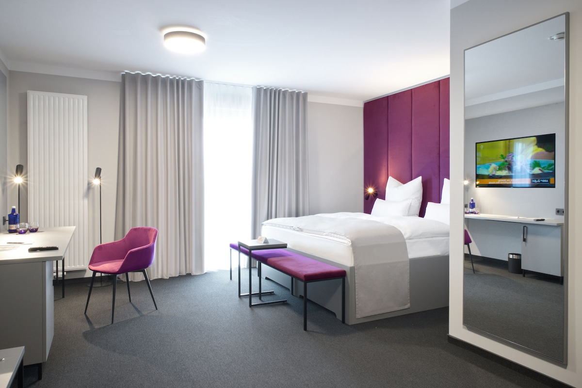 Una habitación de hotel moderna con cama, escritorio, silla, banco, televisor y espejo.