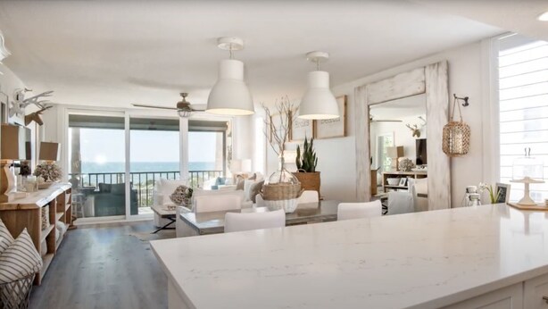 A spacious living area with a large white marble island, white furniture, and pendant lighting.