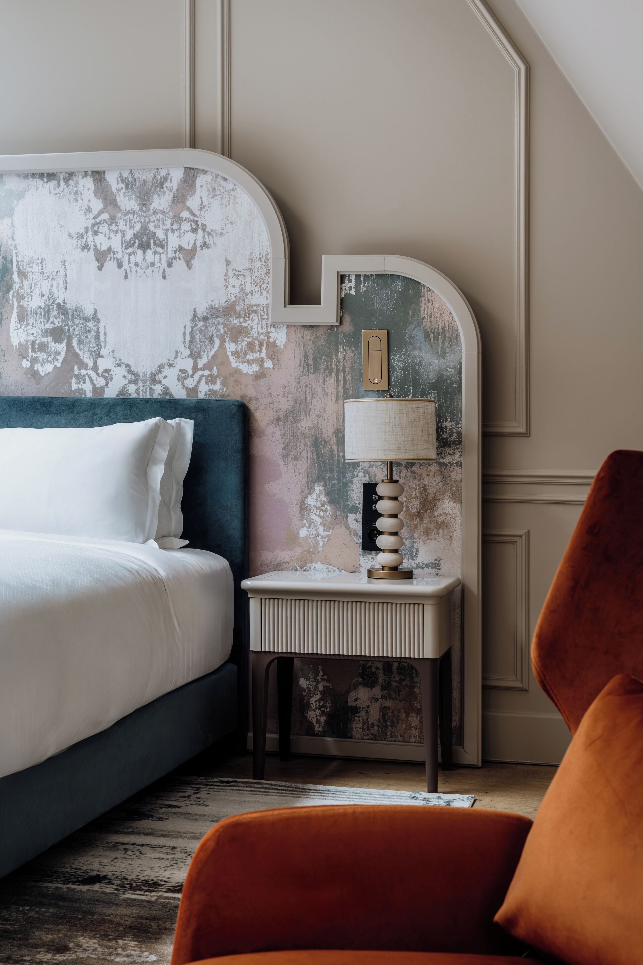 A hotel room with a bed, a nightstand with a lamp, and a chair.