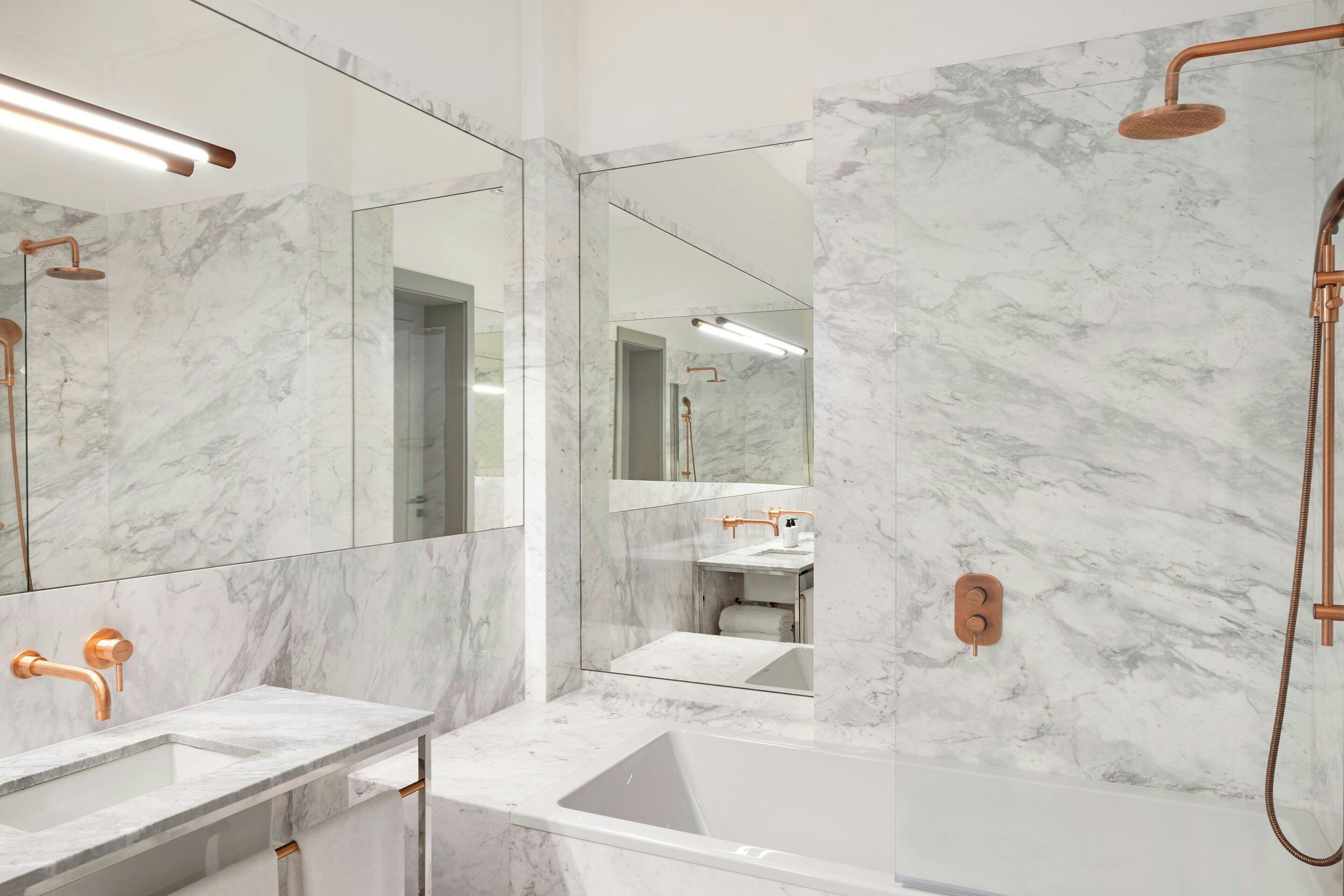 Un baño moderno con paredes de mármol, una bañera y un lavamanos con detalles de cobre.