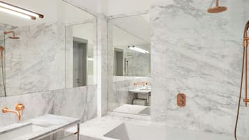 Un baño moderno con paredes de mármol, una bañera y un lavamanos con detalles de cobre.