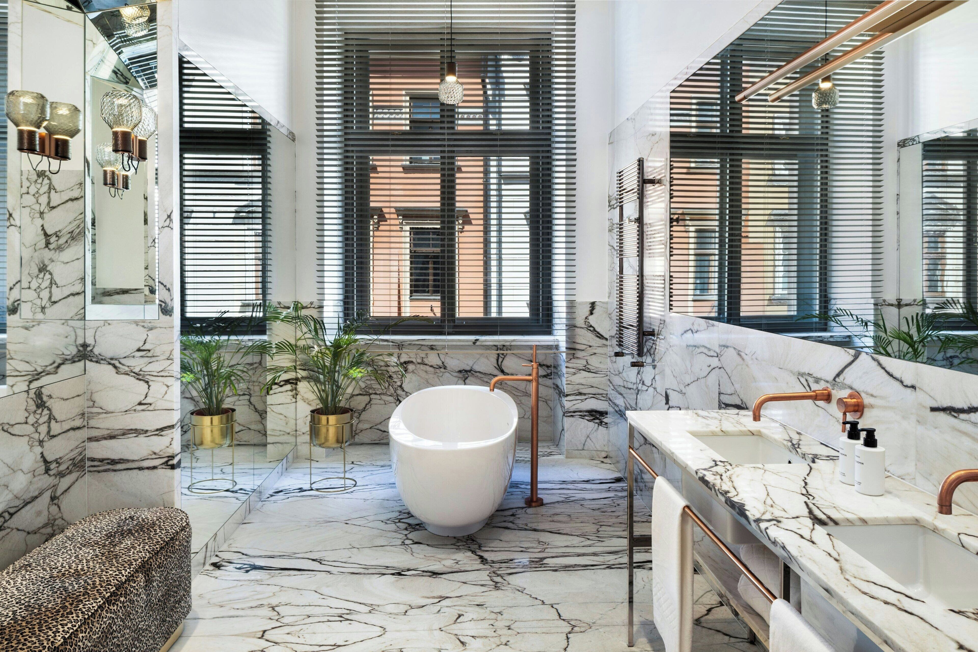 Un baño moderno con una bañera grande, suelo de mármol y ventanas amplias con persianas.