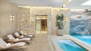 Un área de spa con paredes de piedra, un jacuzzi, sillones de descanso y una cascada.