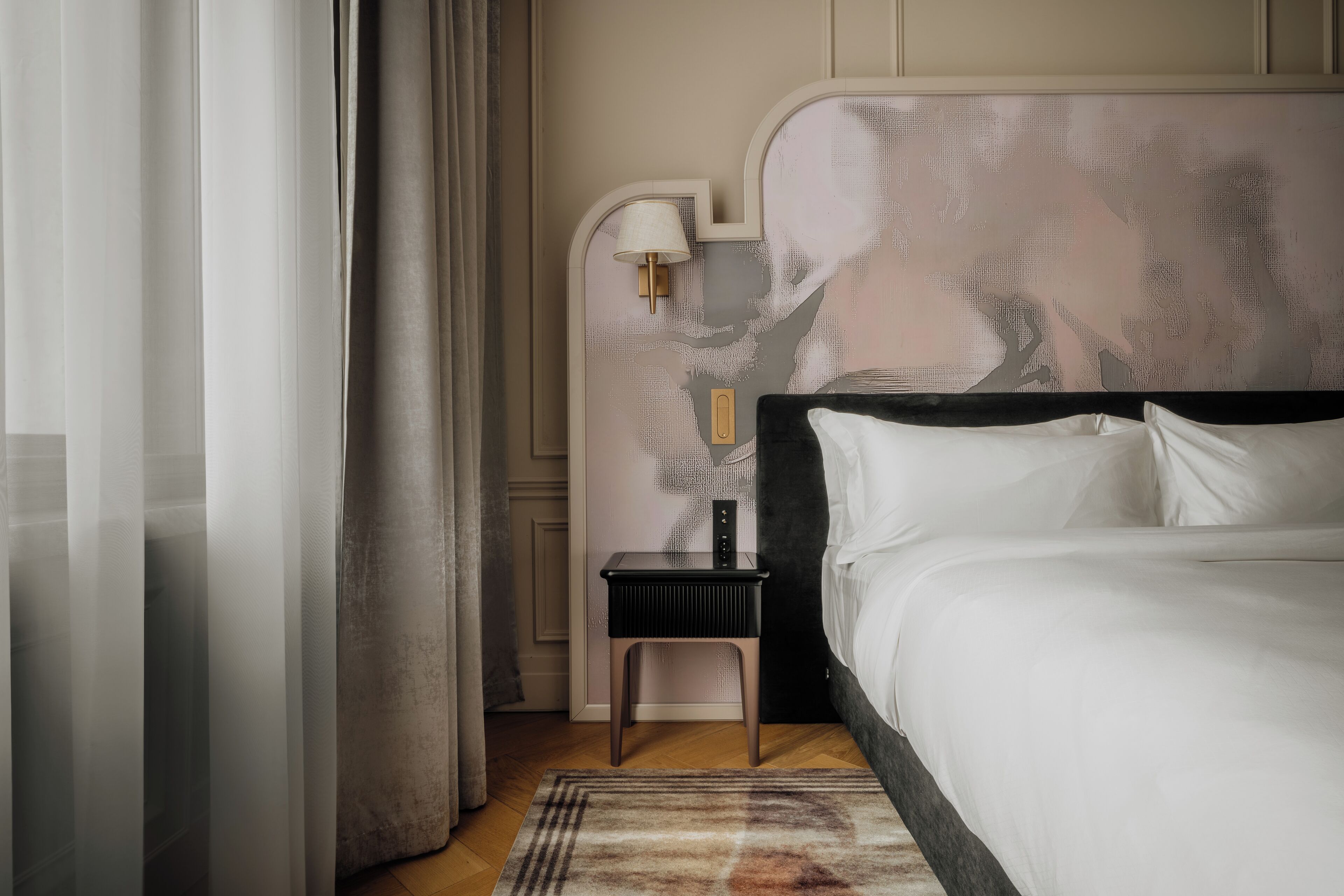 Een hotelkamer met een groot bed, een nachtkastje met een lamp en een hoofdbord met een patroon.