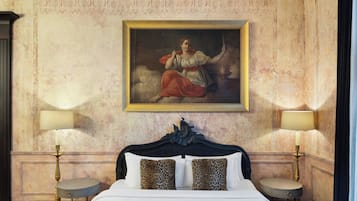 A hotel room with a classic bed, two bedside lamps, and a large framed painting on the wall.