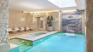 Una piscina moderna en el interior, con una pared de piedra, una bañera de hidromasaje y sillones de descanso.
