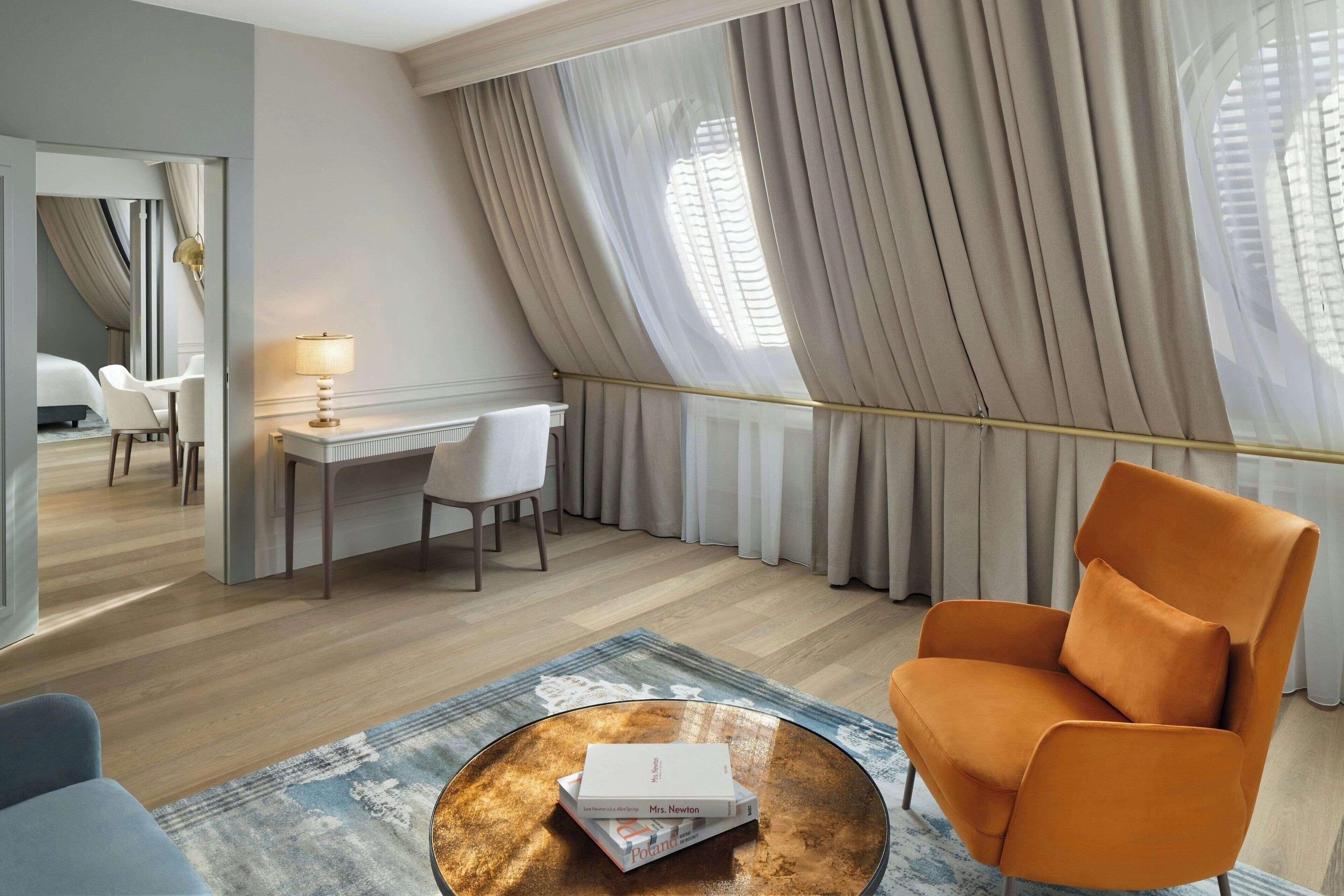 A modern hotel room with a desk, chair, and a large window with curtains.