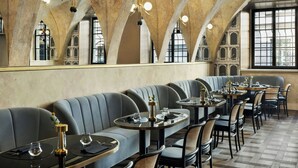Un restaurante con una amplia zona de asientos tipo banco, mesas redondas y un techo alto y abovedado.