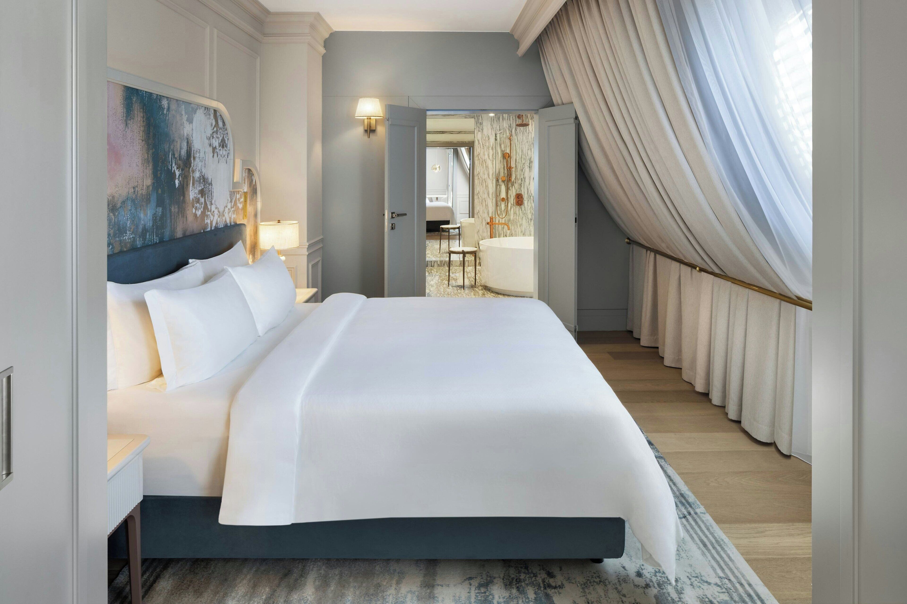 A spacious hotel room with a large bed, a modern bathroom, and a view of the city.