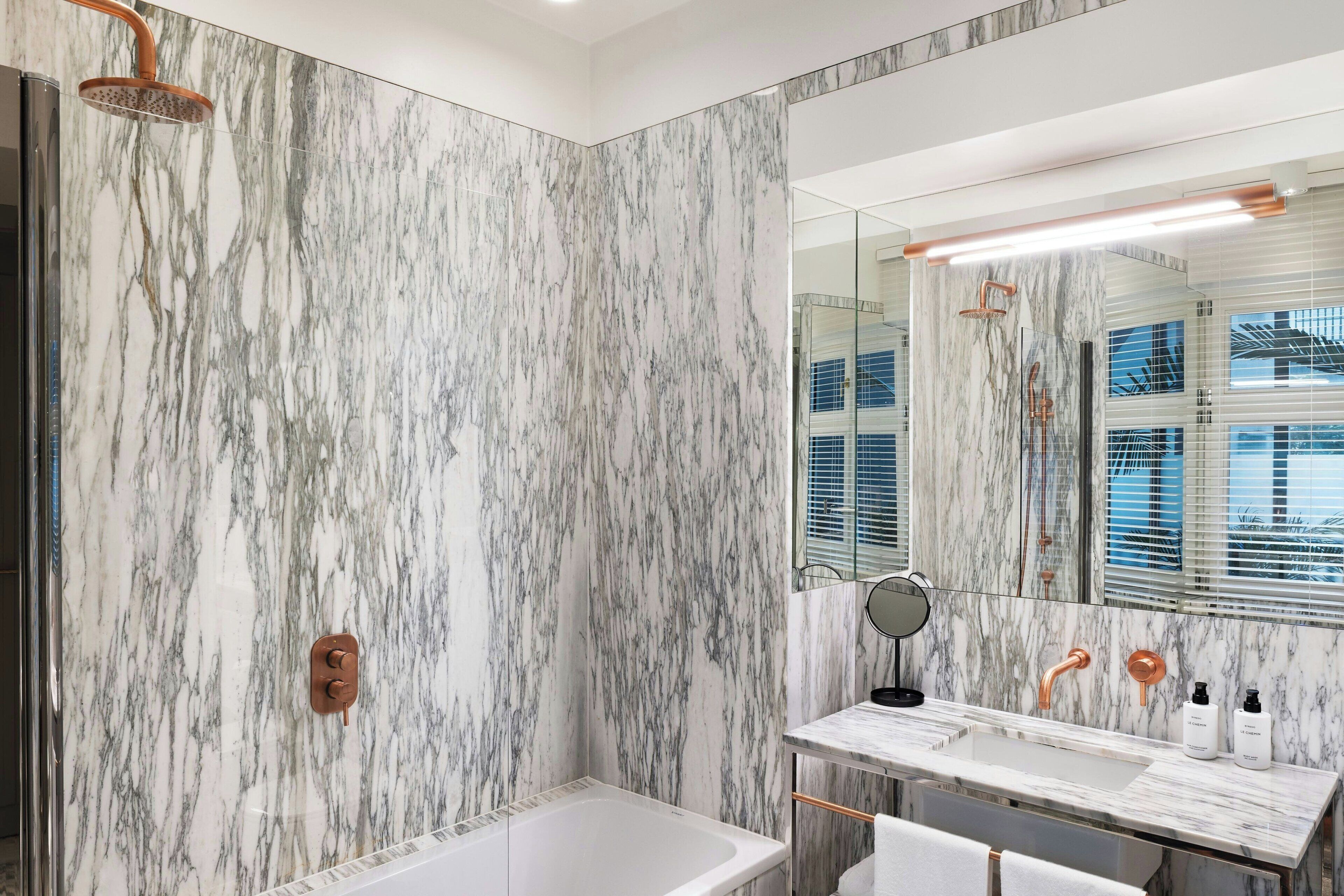 Une salle de bain moderne avec un mur en marbre, une baignoire, un lavabo avec un miroir et une douche.