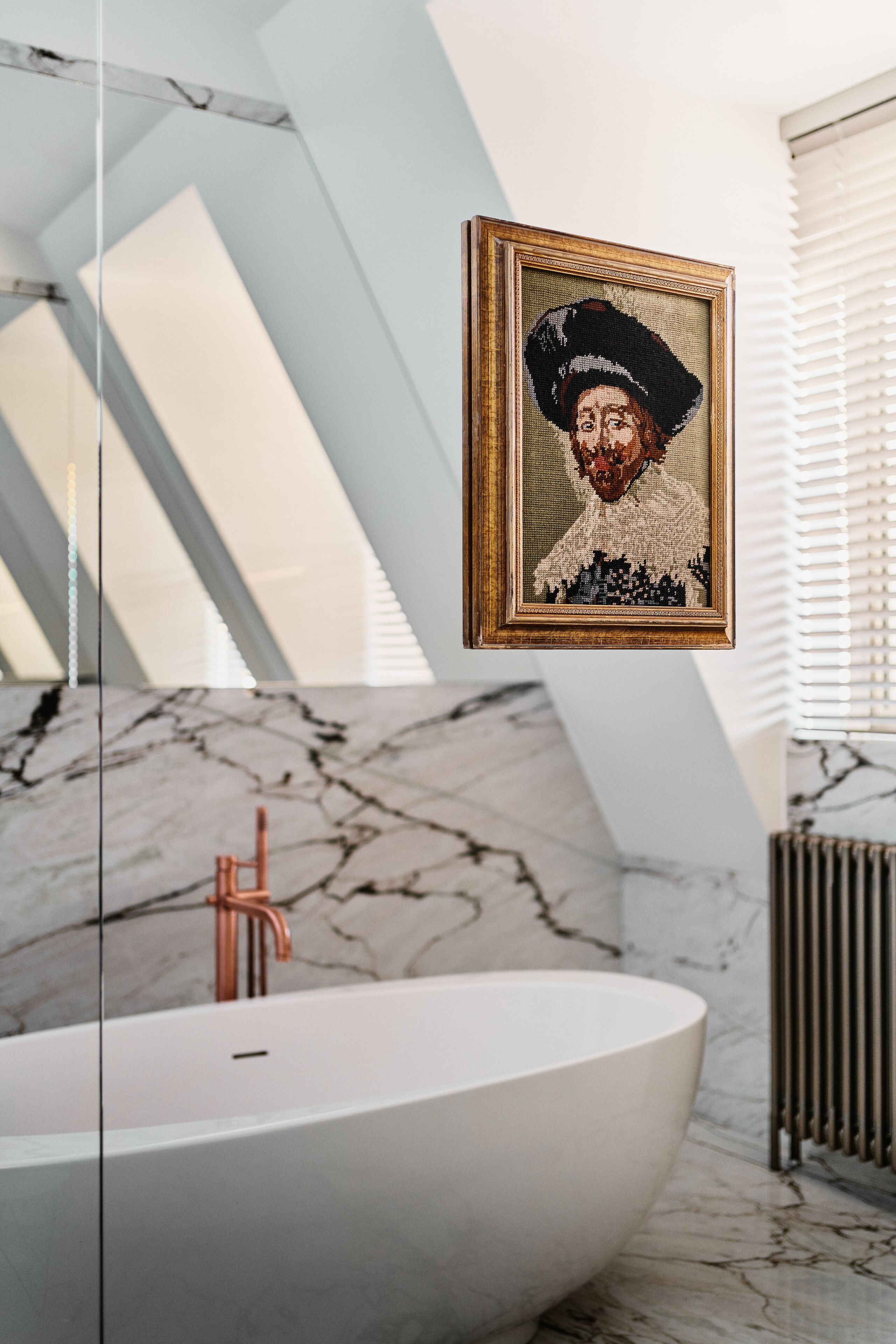 A modern bathroom with a freestanding bathtub, marble flooring, and a framed artwork on the wall.