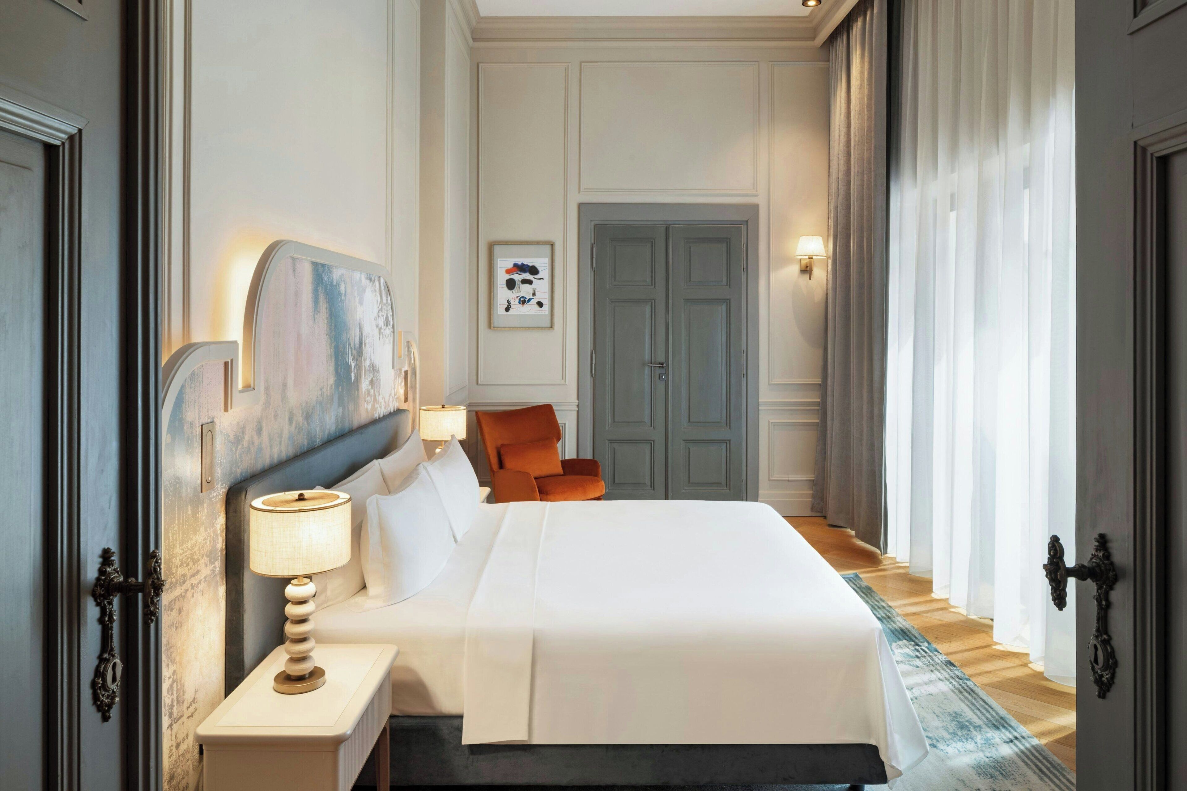 A large bed with a white headboard, a bedside table with a lamp, and a framed picture on the wall.
