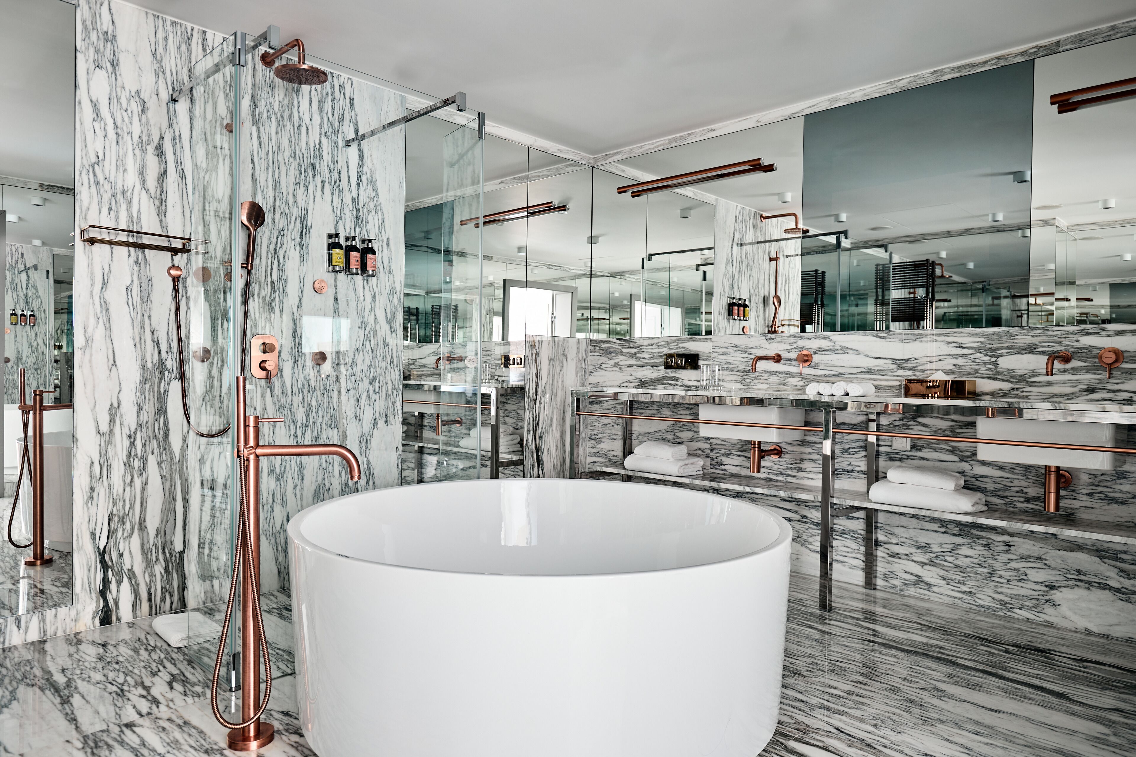 A modern bathroom with a large white bathtub, marble walls, and a glass-enclosed shower area.