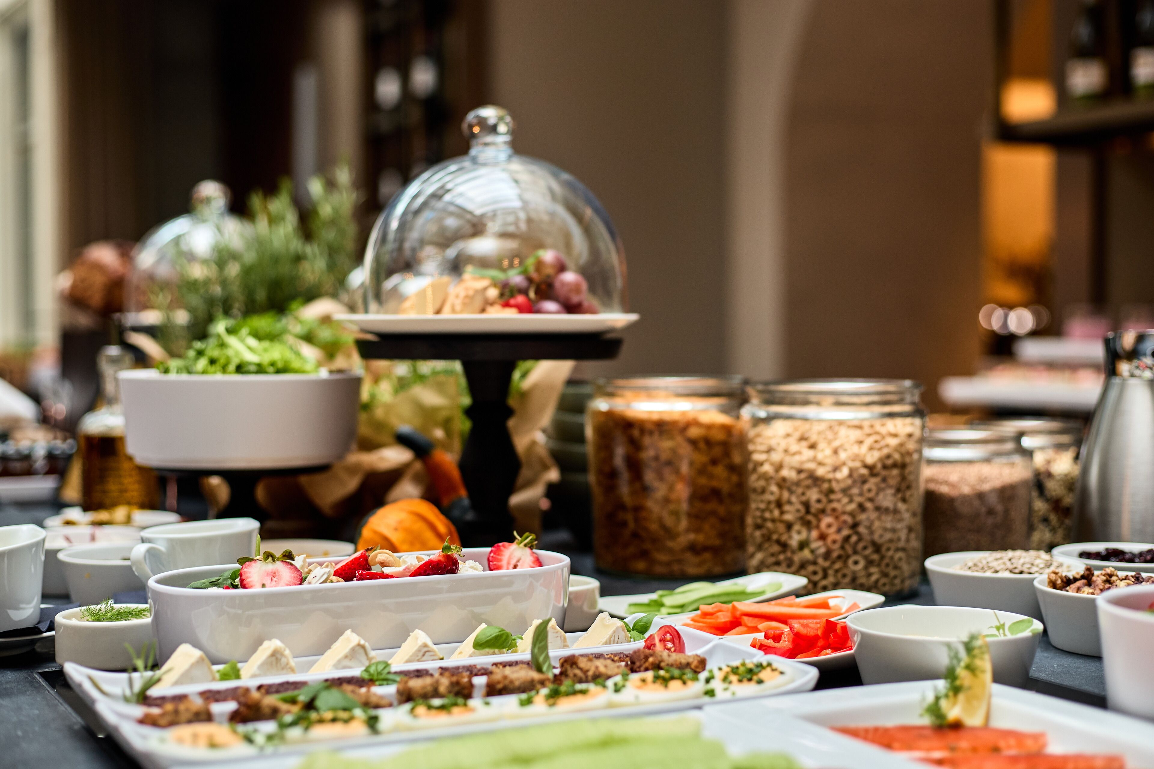 Un buffet con diversi cibi e un cupola di vetro che ricopre un piatto, con barattoli di condimenti sullo sfondo.