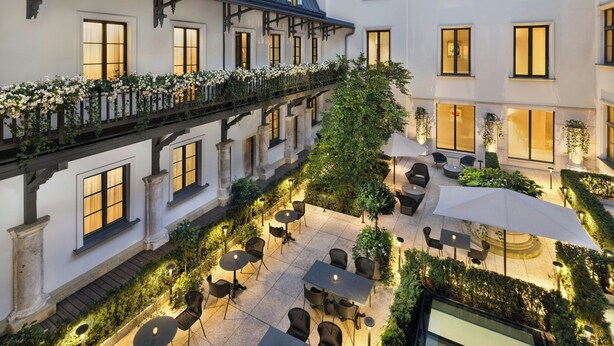 Un patio con mobiliario exterior, una zona techada y un balcón lleno de flores.